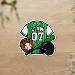 May include: An embroidered patch featuring a green and white pinstriped baseball jersey with the name LIAM and the number 07, a brown baseball glove holding a white baseball with red stitching, and a solid black baseball batting helmet.