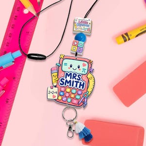 May include: A lanyard featuring a calculator-shaped charm with the text "MRS. SMITH", a pencil, a ruler, and a note saying "2+2=4". Above it are a blue bead, a math-themed cube, and a book charm labeled "Little Reasons". Includes a metal clasp.