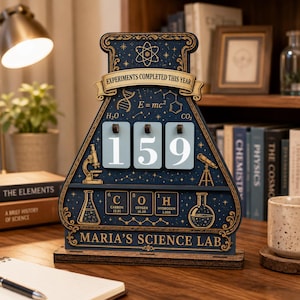 May include: A dark blue, flask-shaped wooden counter with gold accents, featuring the text "EXPERIMENTS COMPLETED THIS YEAR" and "MARIA'S SCIENCE LAB." It displays three flip-style number cards showing 159, alongside scientific icons like a microscope, telescope, DNA strand, and periodic table elements.