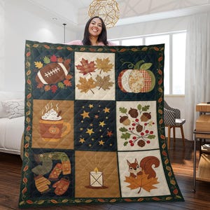 May include: A quilted blanket featuring autumn-themed squares. The squares depict a football, maple leaves, a pumpkin, a mug of hot cocoa, stars, acorns, a scarf and mittens, a candle, and a squirrel. The blanket has a dark green border with leaf accents.