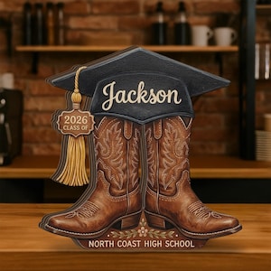 May include: Wooden graduation decoration featuring brown cowboy boots, a black graduation cap with the name "Jackson", and the text "2026 Class of". The base reads "North Coast High School".