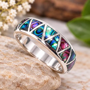 May include: A silver-toned ring featuring a series of triangular inlays made of iridescent abalone shell. The shell segments display vibrant shades of blue, green, and purple, set within a polished metal band with a geometric triangular pattern.