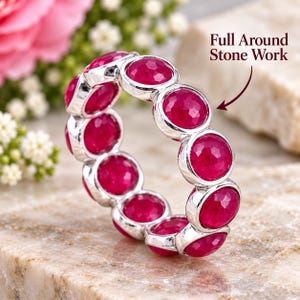 Può includere: Un anello color argento con una fascia continua di pietre rotonde, sfaccettate e di un vibrante rosso rosato. Il testo "Full Around Stone Work" è stampato vicino all'anello, indicando che le pietre circondano l'intera fascia del gioiello.
