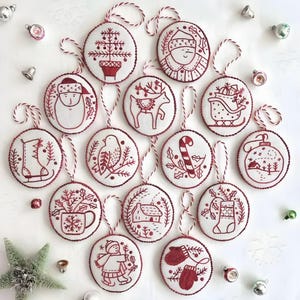 Puede incluir: Una colección de adornos navideños redondos con diseños rojos y blancos. Cada adorno presenta una ilustración festiva diferente, incluyendo a Papá Noel, un reno y un árbol de Navidad. Los adornos tienen ribetes rojos y están ensartados con hilo rojo y blanco.