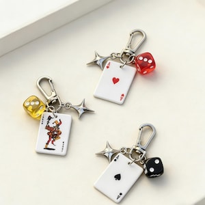 May include: Keyrings with playing card and dice charms. Each keyring features a silver-tone clasp, a star-shaped charm, and a playing card with an ace design. One keyring has a red die, another a yellow die, and the last a black die.
