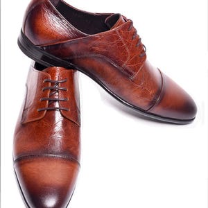 Peut inclure: Une paire de chaussures de ville en cuir marron avec un bout rapporté. Les chaussures ont une fermeture à lacets et une semelle marron foncé. Le cuir présente un aspect texturé avec des variations de couleur.