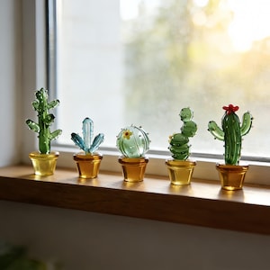以下が含まれることがあります： 木製の窓枠に、琥珀色の鉢に入ったガラス製のサボテンの彫刻が5つ並んでいます。サボテンはさまざまな緑と青の色合いで、1つは赤い花が咲いています。窓は明るく自然な背景を提供しています。
