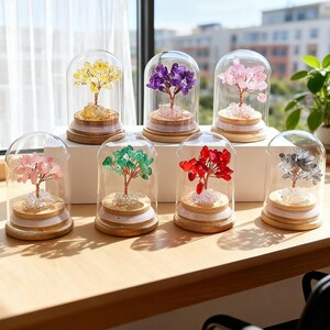 以下が含まれることがあります： 色とりどりのクリスタルで作られたミニチュアツリーを収めた、装飾用のガラスドームのコレクション。ツリーは、黄色、紫、ピンク、緑、赤、銀色のクリスタルでできており、木製の台座にセットされています。ドームは明るい色の木製の表面に展示されています。