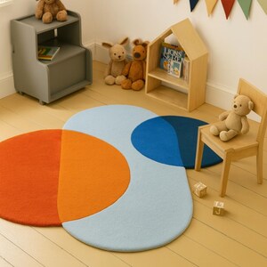 May include: A child's room with a vibrant, geometric rug in shades of orange, light blue, and dark blue. The room includes a wooden chair, a small bookshelf, and soft toys. A colourful pennant banner is suspended on the wall.