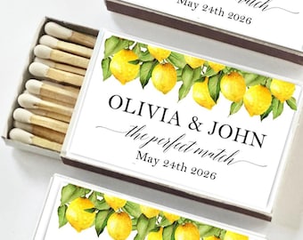 May include: Three matchboxes with a white background. Each box features a lemon and leaf design at the top, with the text "OLIVIA & JOHN the perfect match May 24th 2026". One box is open, revealing wooden matches.