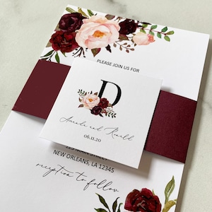 May include: Wedding invitation suite featuring floral accents in burgundy and blush tones. The invitation includes the text "PLEASE JOIN US FOR", the names "Ancale and Ronald", and the date "06.11.20". The address "125 MAIN STREET, NEW ORLEANS, LA 12345" is also included.