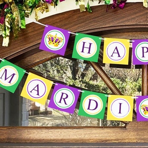 May include: A festive Mardi Gras banner with the words "HAPPY MARDI GRAS" in green, purple, and yellow squares. The banner is strung across a wooden door, with a garland of green, purple, and gold tinsel above.