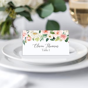 May include: A white place card with a floral design in shades of pink and green. The text "Olivia Thomas Table 1" is printed in black.