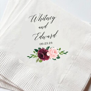 May include: White paper napkins with the names "Whitney and Edward" and the date "09.23.24" printed in black script. A floral design with burgundy and pink roses and green leaves is below the names.