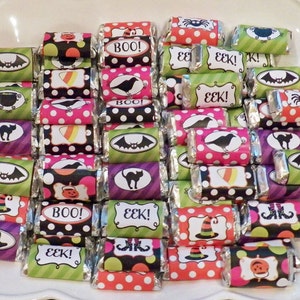 May include: A collection of Halloween-themed candy bars with colorful wrappers. The wrappers feature various designs, including bats, spiders, and the words "BOO!" and "EEK!" The candies are arranged on a white plate, creating a festive display.