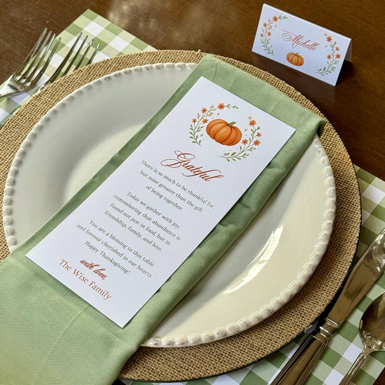 K&ouml;nnte beinhalten: Herbstliche Tischdekoration mit wei&szlig;em Teller, gr&uuml;ner Serviette und Tischkarte. Die Tischkarte und das Men&uuml; zeigen eine K&uuml;rbisillustration und das Wort "Grateful". Das Set beinhaltet einen Jutenteller, Besteck und eine gr&uuml;n-wei&szlig; karierte Tischdecke.