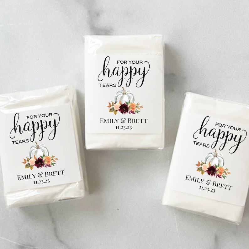 May include: Three white tissue packs with labels. The labels read "FOR YOUR happy TEARS" in script above a pumpkin and floral design. The names "EMILY & BRETT" and the date "11.23.23" are below the design.