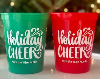May include: Two plastic cups, one green and one red, with white text that reads "Holiday CHEER with the Wise Family." The cups are likely for a holiday celebration.