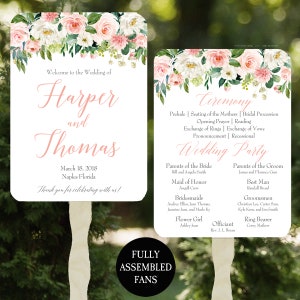 May include: Two white wedding fans with floral designs in pink and white, featuring the names "Harper and Thomas" and wedding details. One fan lists the ceremony order and wedding party. The fans are fully assembled.