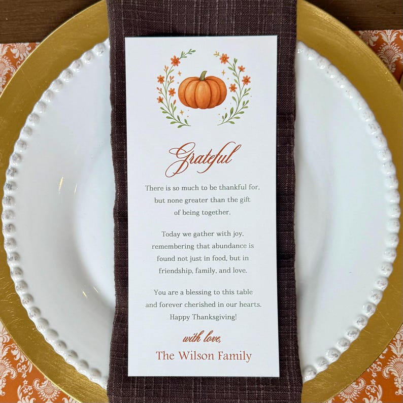 K&ouml;nnte beinhalten: Ein Thanksgiving-Gedeck mit einem wei&szlig;en Teller, einem goldenen Untersetzer und einer braunen Serviette. Eine Karte mit einer K&uuml;rbisillustration und dem Wort "Grateful" liegt auf der Serviette. Die Karte enth&auml;lt eine Thanksgiving-Nachricht.