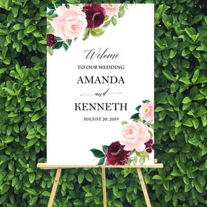 May include: A white wedding welcome sign with burgundy and pink floral illustrations. The sign reads "Welcome to our wedding Amanda and Kenneth August 20, 2019".