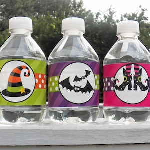 May include: Three clear water bottles with white caps, each featuring a Halloween-themed label. The labels display a witch's hat, bats, and witch's legs, with polka dot and striped backgrounds. The bottles are displayed outdoors.