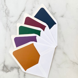 May include: Five white envelopes with colored card inserts. The inserts are in shades of purple, green, burgundy, and navy blue. The bottom insert is a solid brown color.