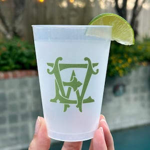 May include: A white plastic cup with a green monogram of the letters "EW" printed on the side. A lime wedge is placed on the rim of the cup.
