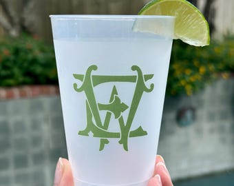 May include: A white plastic cup with a green monogram of the letters "EW" printed on the side. A lime wedge is placed on the rim of the cup.