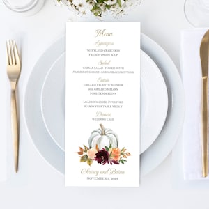 May include: A wedding menu card with a white pumpkin and floral design. The menu lists appetizers, salad, entrees, and dessert. The names "Christy and Brian" and the date "November 5, 2024" are printed at the bottom.