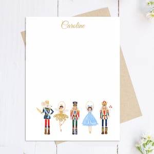 May include: White stationery with a watercolor illustration of five Nutcracker characters. The word "Caroline" is written in gold script at the top. The stationery is on a brown envelope.