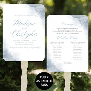 May include: A wedding program fan with a watercolor background in shades of blue. The fan features the names Madison and Christopher, the wedding date, and the wedding party details. The text "Fully Assembled Fans" is printed on the bottom of the fan.