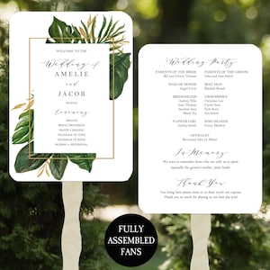 May include: Wedding ceremony program fans with tropical leaves and gold accents. The fans feature the names Amelie and Jacob, the wedding date, and a list of ceremony events. The back of the fans includes the wedding party names and a thank you message.