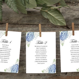 May include: Three white cards with blue and white floral designs and black text. The cards are labeled "Table 1", "Table 2", and "Table ". Each card lists a group of names.