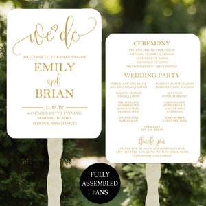May include: Two white wedding fans with gold text. One fan reads "We do" and details the wedding of Emily and Brian. The other fan lists the ceremony order and wedding party. The fans are fully assembled.
