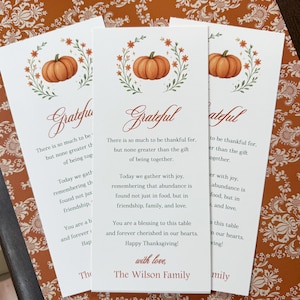 K&ouml;nnte beinhalten: Drei wei&szlig;e Thanksgiving-Karten mit einer K&uuml;rbis-Illustration und dem Wort "Grateful" in Schreibschrift. Die Karten enthalten Texte &uuml;ber Dankbarkeit und Familie, mit den S&auml;tzen "Happy Thanksgiving!" und "The Wilson Family."
