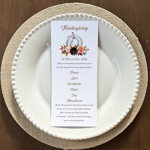 May include: A Thanksgiving-themed place setting featuring a white plate with a beaded rim, a burlap placemat, and a printed card. The card reads "Thanksgiving" with a pumpkin and floral design, and lists sentiments like "Peace" and "Love."