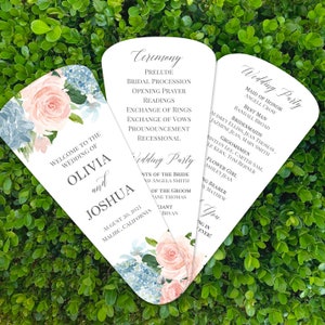 May include: Wedding ceremony program fans with floral designs. The front features a watercolor floral design with pink roses and blue hydrangeas. The back features the wedding ceremony schedule and wedding party names. The text reads "Welcome to the Wedding of Olivia and Joshua, August 20, 2023, Malibu, California."