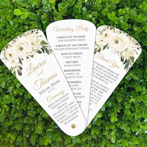 May include: White wedding fan with floral design and gold text. The fan includes the names Lauren and Thomas, the wedding date, and the wedding party.