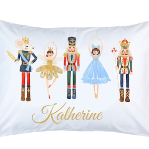 May include: White pillowcase featuring watercolor illustrations of characters from The Nutcracker ballet. The design includes a mouse king, a ballerina, a nutcracker, and a ballerina in a blue dress. The name "Katherine" is written in gold script.