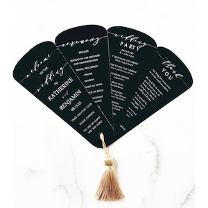 May include: Black and white wedding ceremony program fan with a gold tassel. The fan is folded and has a welcome to the wedding to Katherine and Benjamin on the front. The ceremony details are on the left side and the wedding party details are on the right side. The back of the fan says thank you.