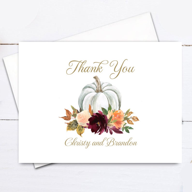 May include: A white greeting card with the words "Thank You" in elegant gold script. A watercolor illustration of a white pumpkin and colorful flowers adorns the card. The names "Christy and Brandon" are printed below the floral arrangement.