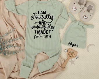 May include: A light green baby outfit set featuring a ribbed jumpsuit with the text "I AM Fearfully and wonderfully MADE psalm 139:14". The set includes a matching hat, bear-shaped slippers, and a wooden rattle.