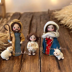 Op de afbeelding: Gehaakte kerststal met Jozef, Maria en een kind, elk met gedetailleerde gelaatstrekken en kleding. Jozef houdt een staf vast en staat met een schaap. Maria draagt een blauwe mantel. Het kind houdt een lam vast.