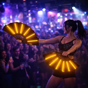 Pode incluir: Uma pessoa segura dois leques dobráveis ​​castanhos escuros abertos, iluminados com luzes LED amarelas brilhantes, em uma boate. Os leques estão abertos, com as luzes criando um padrão radiante. A pessoa está vestindo um top preto com lantejoulas e shorts pretos.