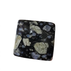 May include: A square-shaped polished stone cabochon featuring a dark black base color with embedded angular inclusions in shades of light gray, off-white, and pale blue. The surface has a smooth, reflective finish with a distinct mottled texture.