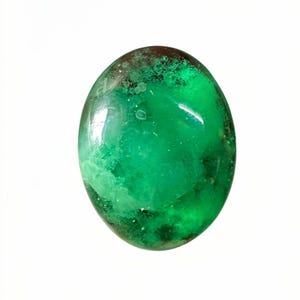 Può includere: Una gemma cabochon di forma ovale caratterizzata da un vibrante colore verde smeraldo traslucido con inclusioni nuvolose interne e macchie verde scuro su tutta la superficie lucida, liscia e arrotondata della pietra.