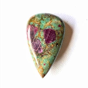 Può includere: Una gemma a forma di goccia. La pietra presenta una base verde vibrante con macchie marroni e inclusioni rosso scuro. La superficie lucida riflette la luce, evidenziando i motivi naturali. Circa 4 cm di lunghezza.