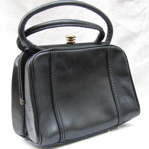 May include: A black leather handbag with a top handle and a gold metal clasp. The bag has a rectangular shape and is decorated with stitching.