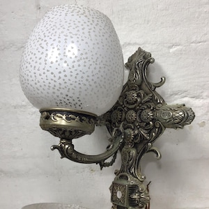May include: A vintage wall sconce with ornate metalwork and two white glass shades with a speckled pattern.